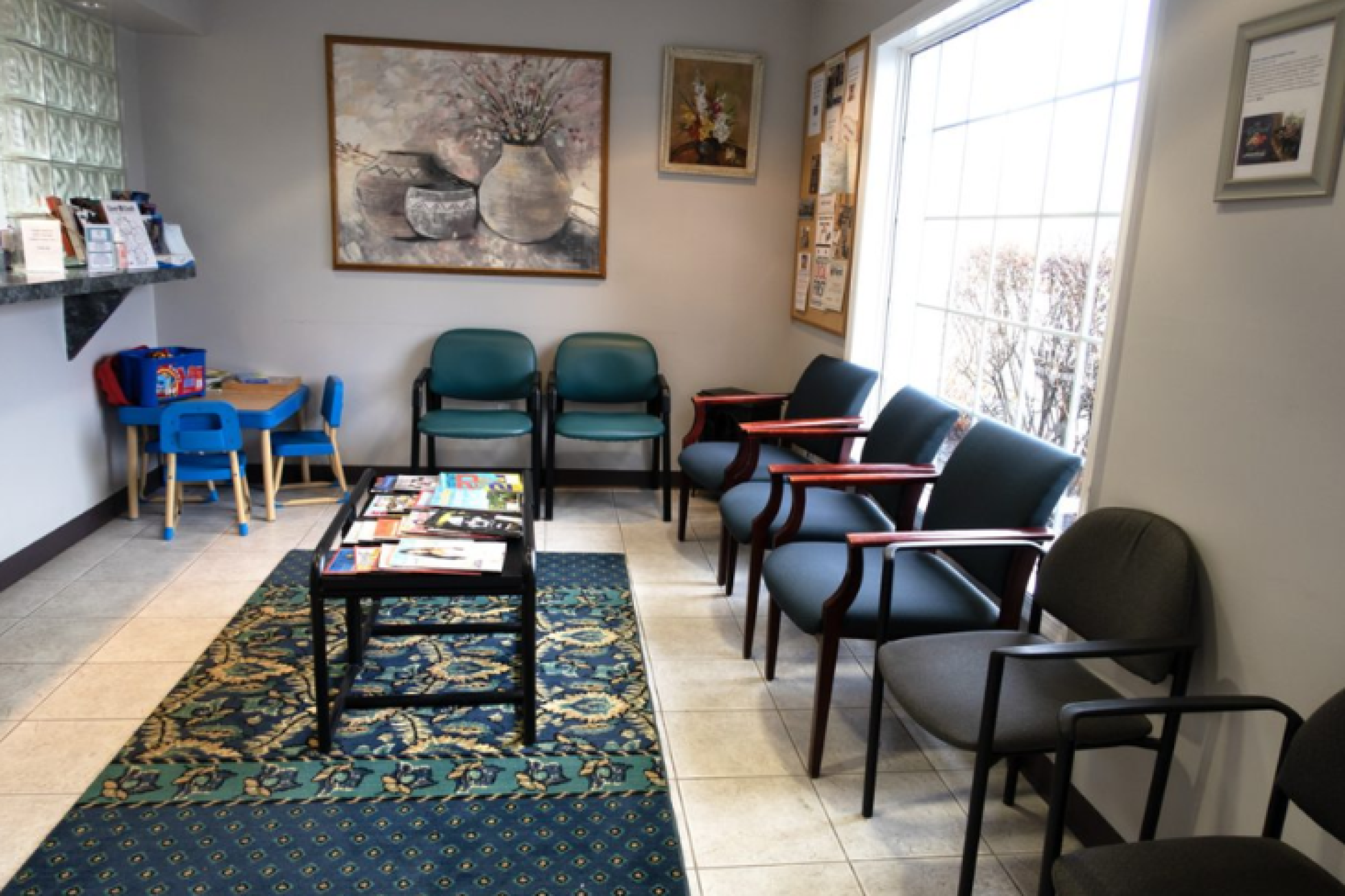 The waiting room of a dental clinic featuring a row of chairs, a children's play area, and a table with reading materials.