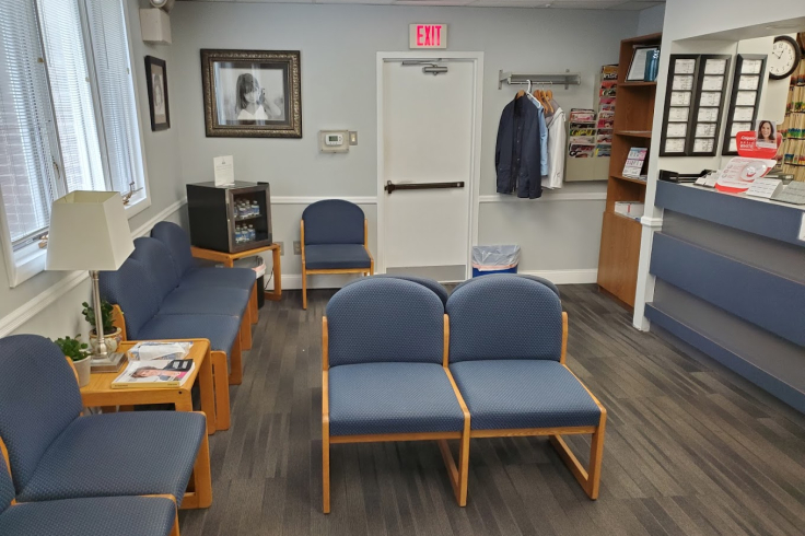 The waiting area of a dental clinic featuring blue chairs, a small coat rack with clothes, a coffee station, and a reception desk with brochures.