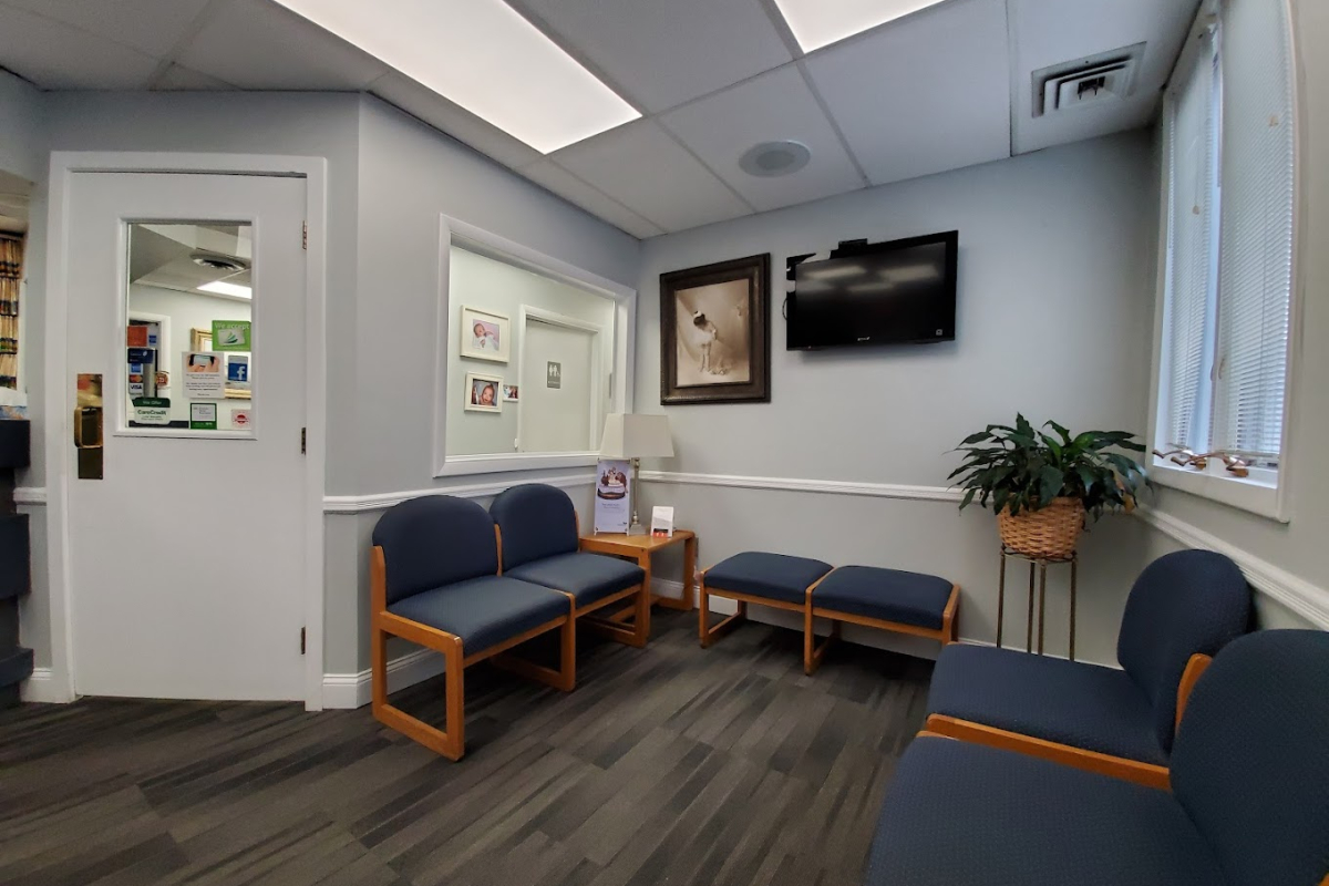 The waiting room of a dental clinic featuring blue cushioned chairs, framed artwork, and a wall-mounted television.
