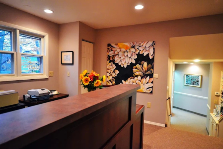 The interior of a dental clinic reception area featuring a wooden desk with flowers and decorative artwork on the walls.