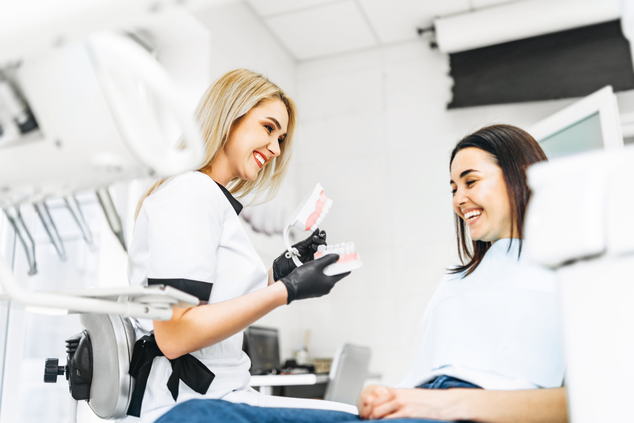 A dentist shows a dental model to a smiling patient in a clinic setting.