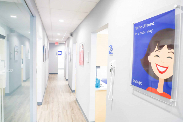 Bright, modern dental clinic hallway with a cheerful wall poster reading "We're different. In a good way." and room number 2 visible.