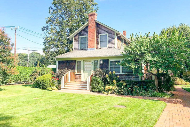 A charming two-story house with a brick chimney, surrounded by a well-maintained lawn and garden under a clear blue sky.