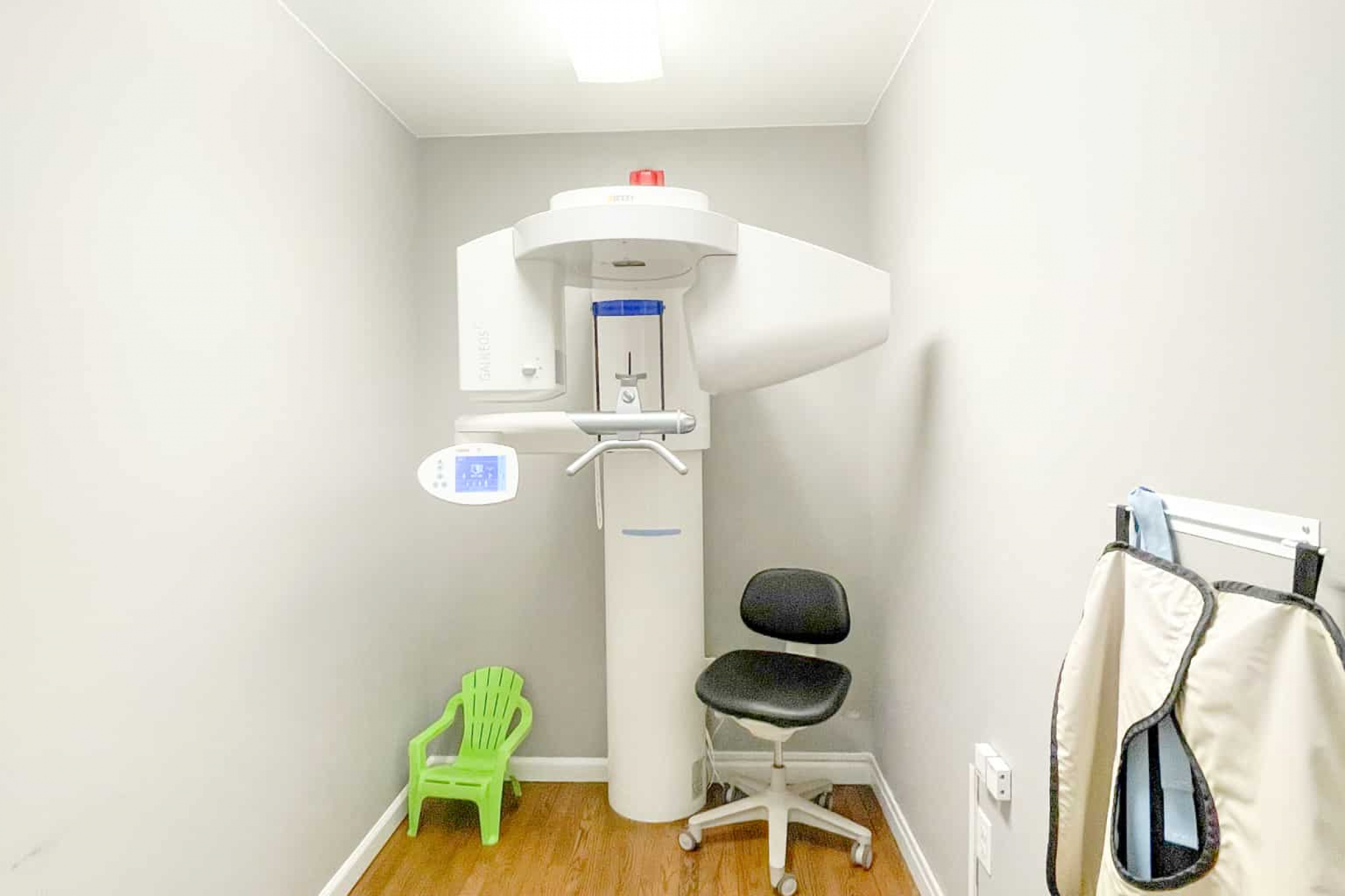 A modern dental panoramic X-ray machine is positioned in a specialized room with a wooden floor and equipped seating.