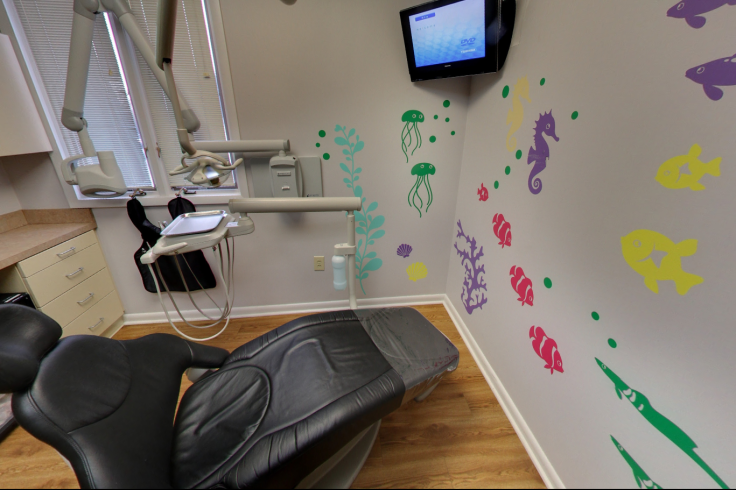 A modern dental examination room with colorful sea creature wall decorations and a mounted flat-screen TV.