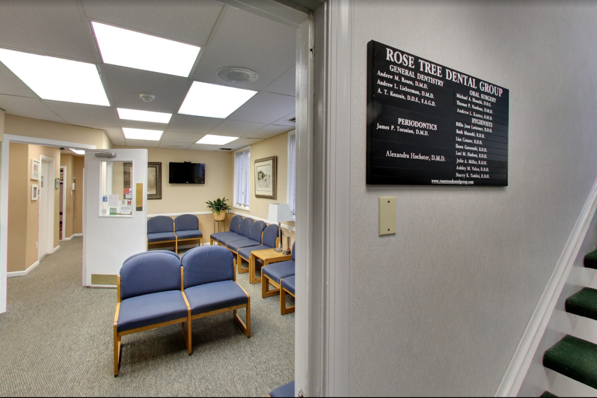 The waiting room of Rose Tree Dental Group features comfortable blue seating and a wall-mounted sign listing the names of dental professionals.