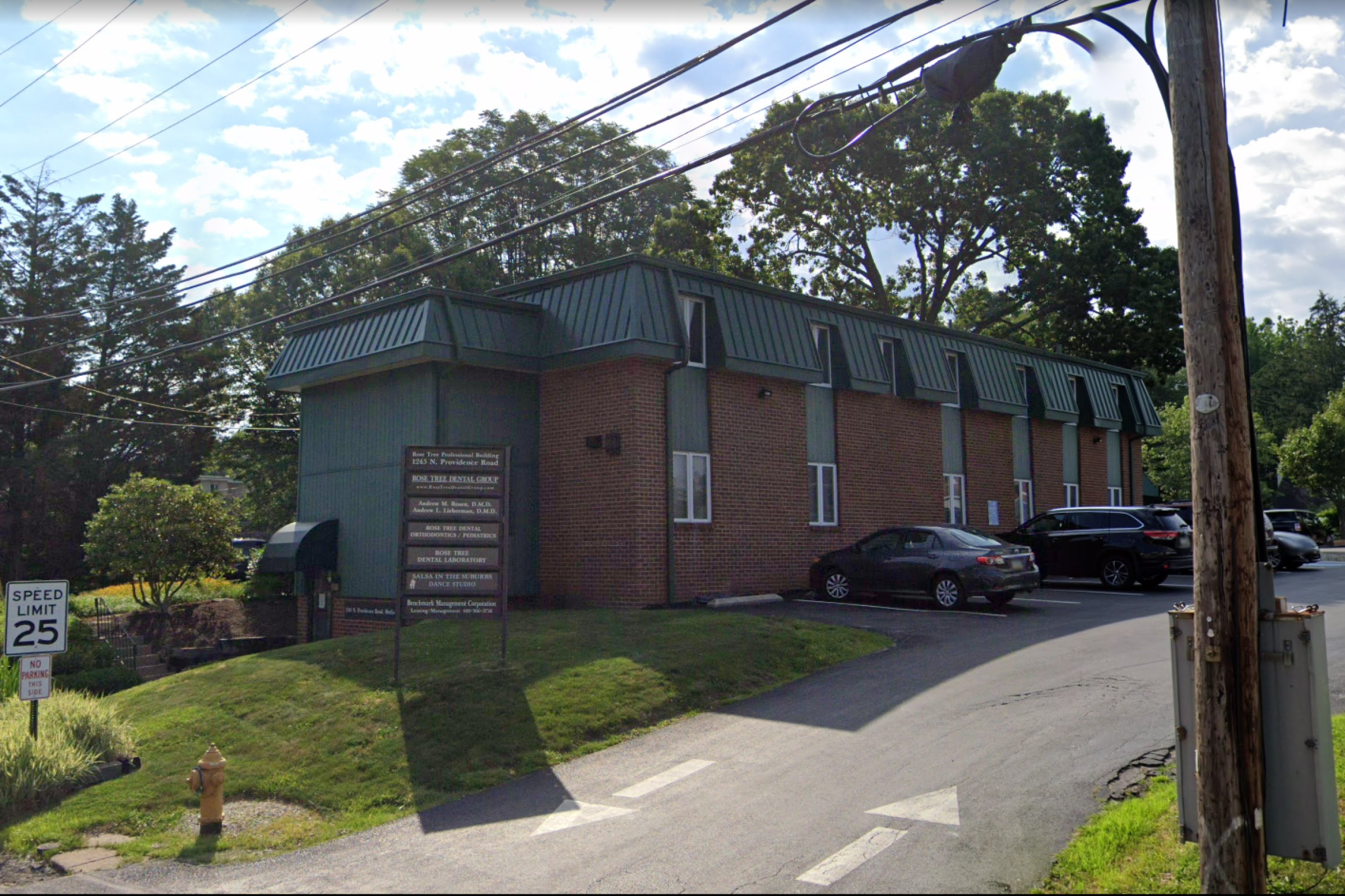 The exterior of "Rock The Dental Group" building, a two-story brick structure with parked cars and signage, viewed from the street.